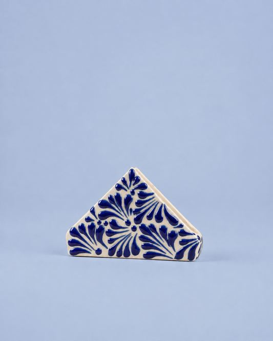 A small triangular ceramic tile with a blue floral pattern on an off-white background, set against a solid light blue backdrop.