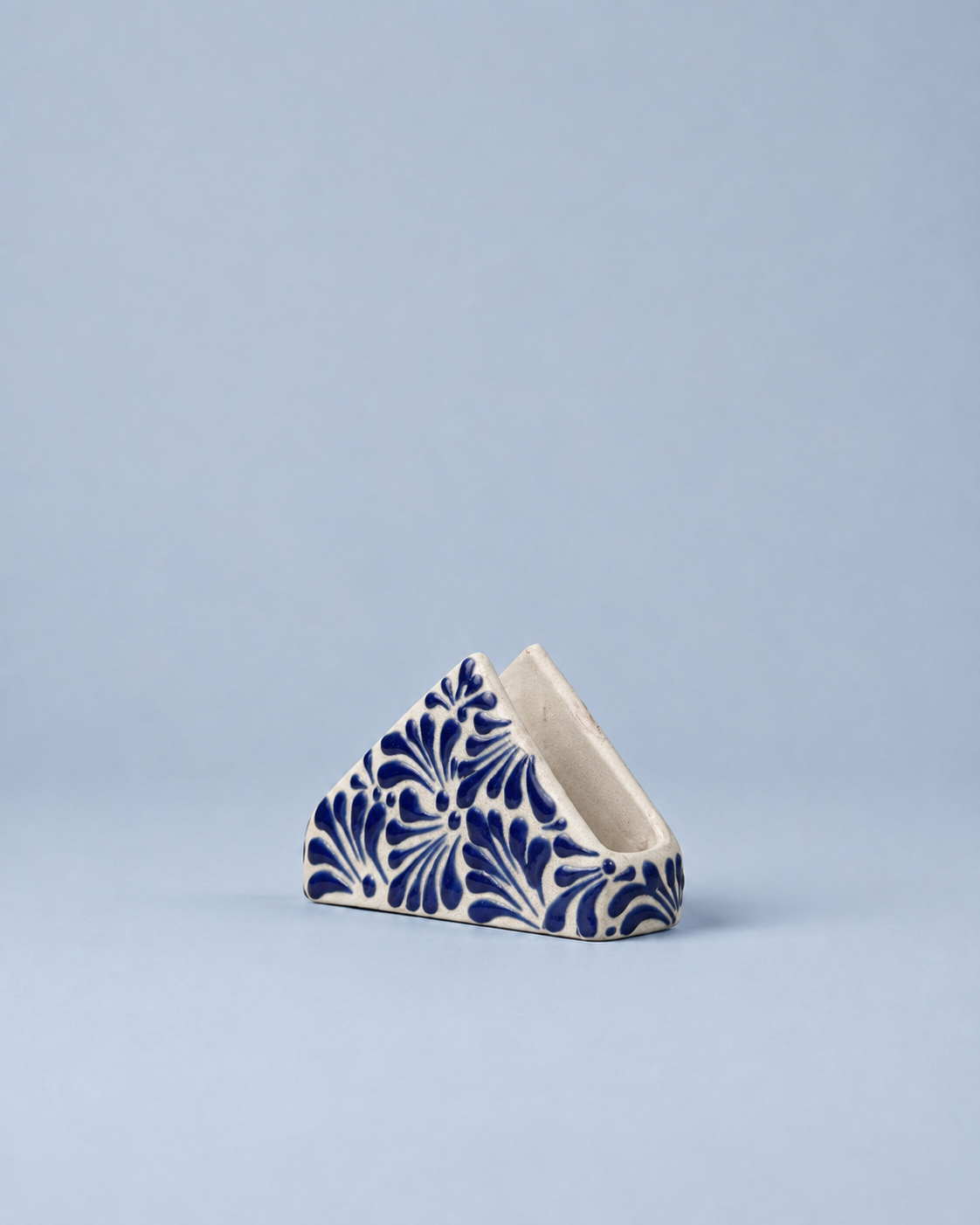 A small triangular ceramic container with a blue and white floral pattern, set against a solid light blue background.