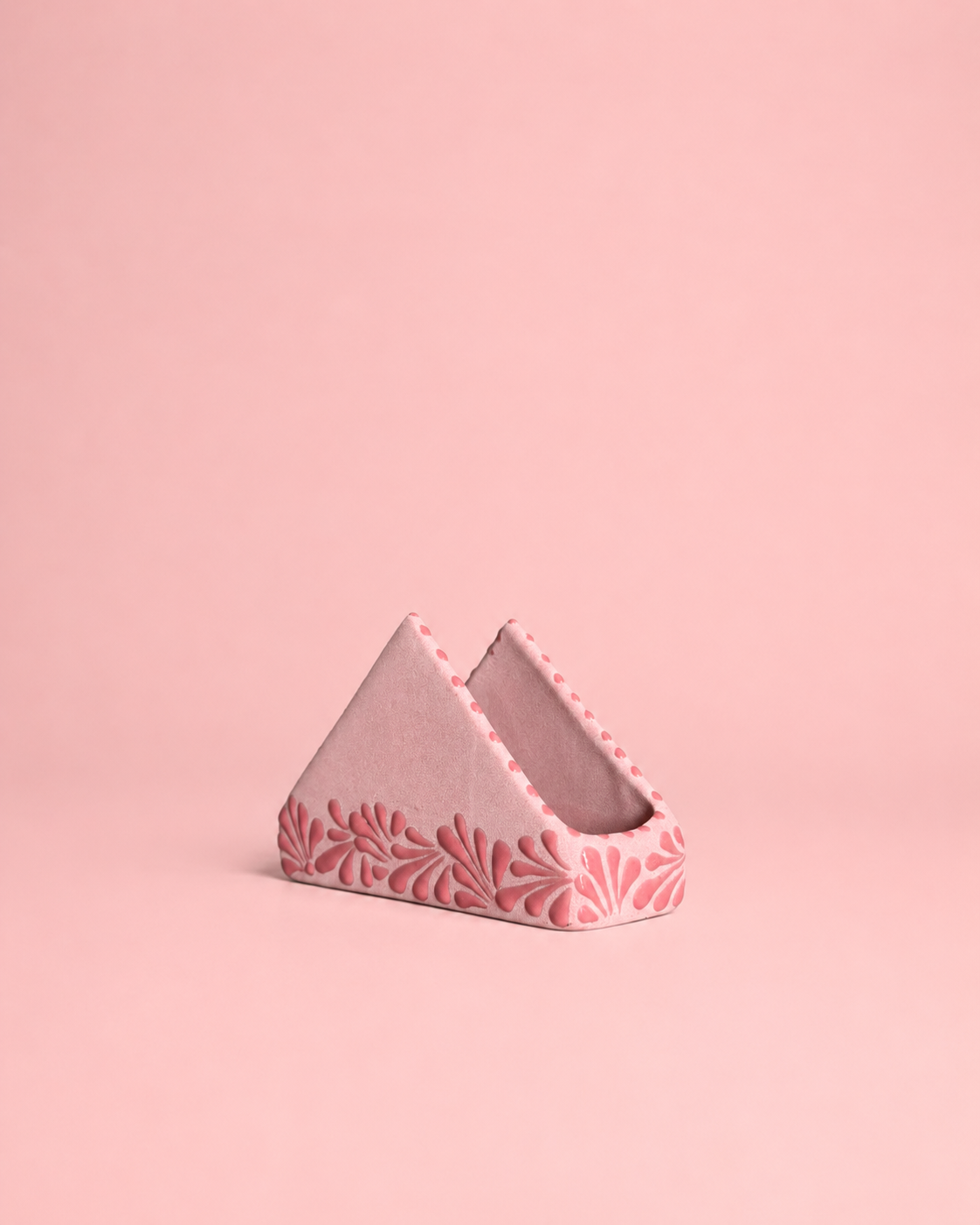 Triangular pink ceramic napkin holder with floral patterns on a pink background