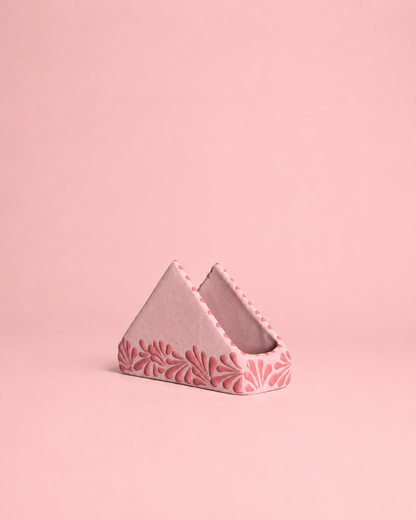 Triangular pink ceramic napkin holder with floral patterns on a pink background