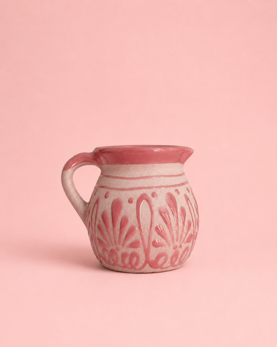 A small ceramic mug with a pink and white floral pattern, set against a solid pink background.