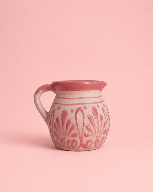 A small ceramic mug with a pink and white floral pattern, set against a solid pink background.
