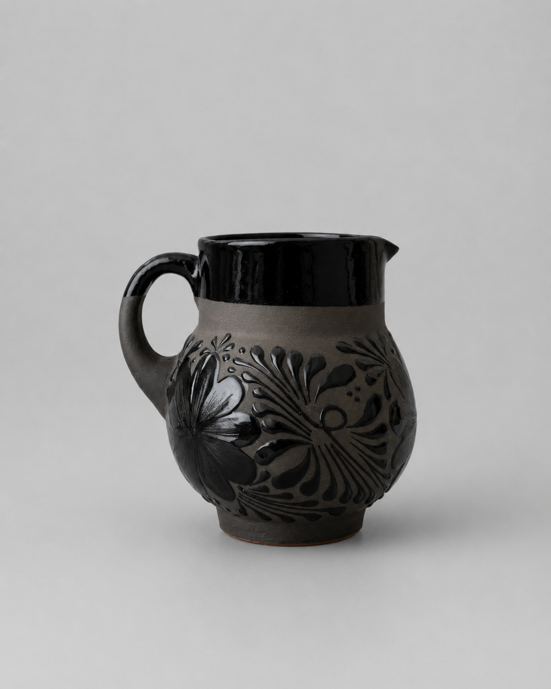 Black ceramic pitcher with floral patterns on a gray background