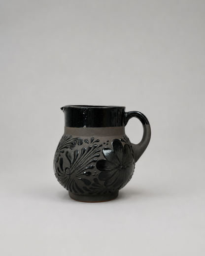 Black ceramic pitcher with floral patterns on a light gray background