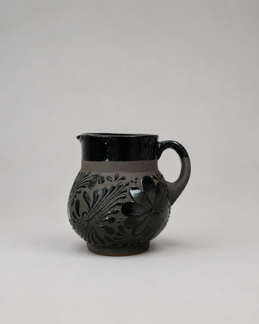 Black ceramic pitcher with floral patterns on a light gray background
