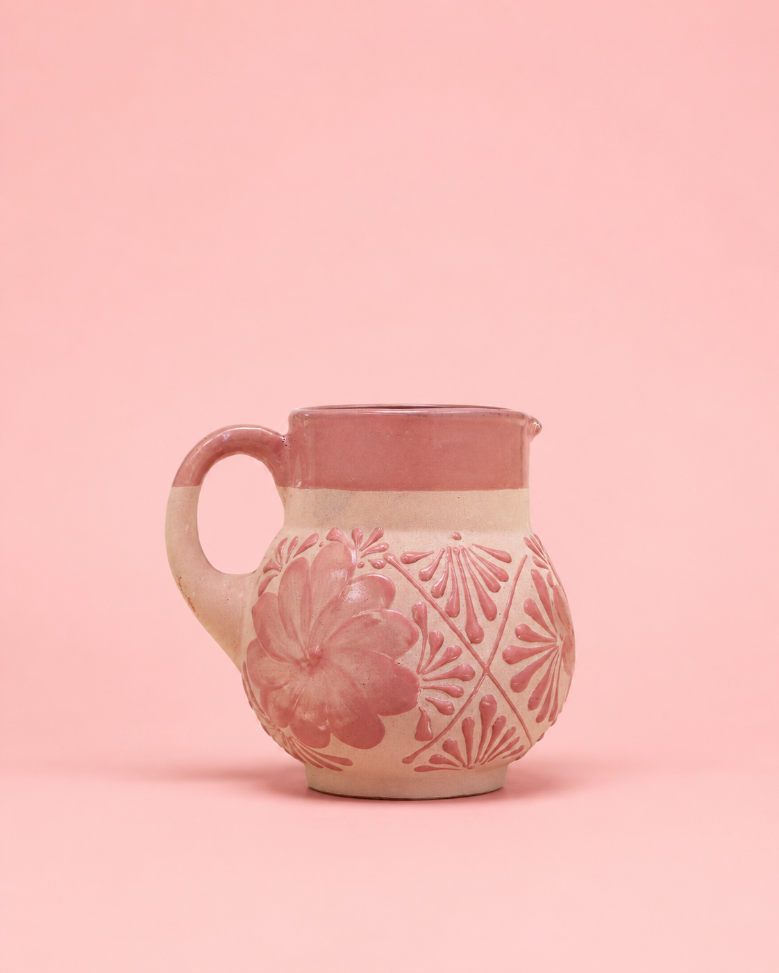 Pink ceramic pitcher with floral patterns on a pink background