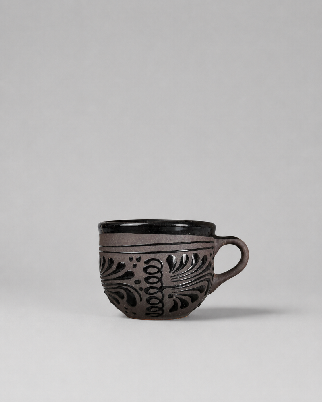 Black ceramic mug with floral patterns on a gray background