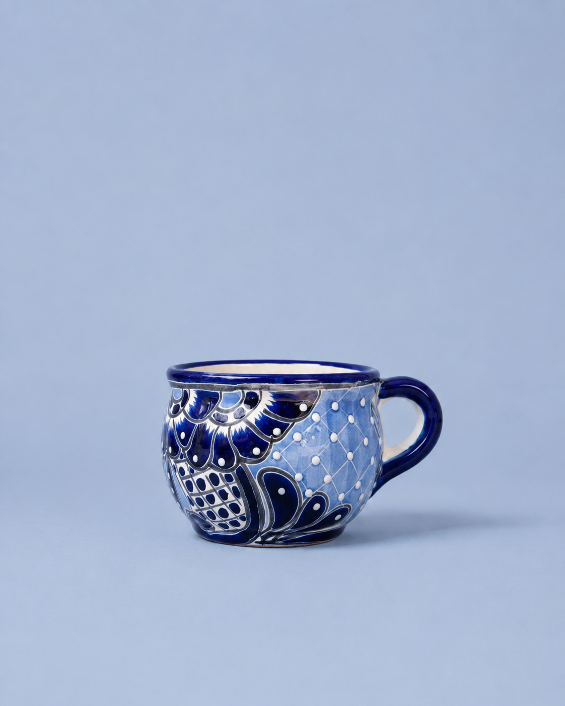 A small ceramic coffee cup with a blue and white hand-painted floral pattern, set against a solid light blue background.