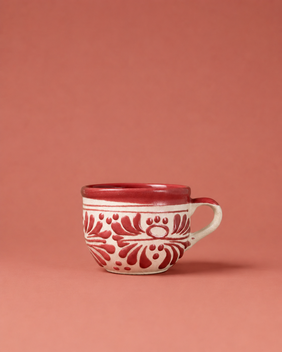Red ceramic mug with white floral patterns on a pink background