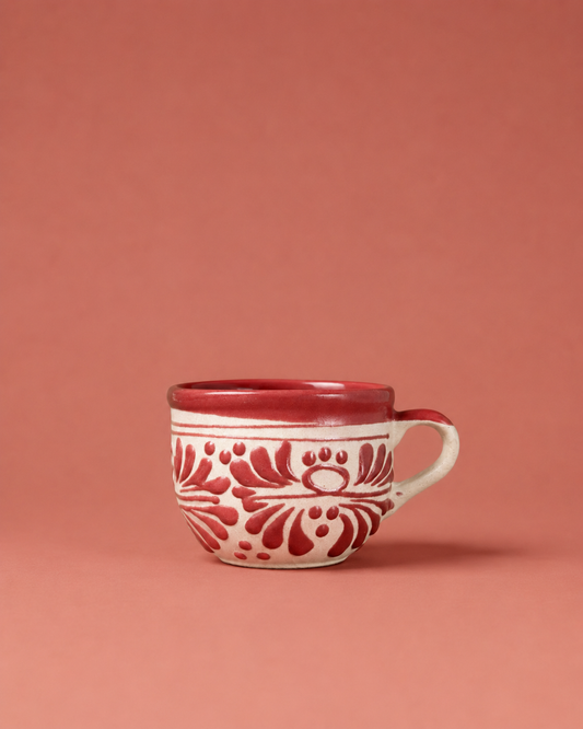 Red ceramic mug with white floral patterns on a pink background