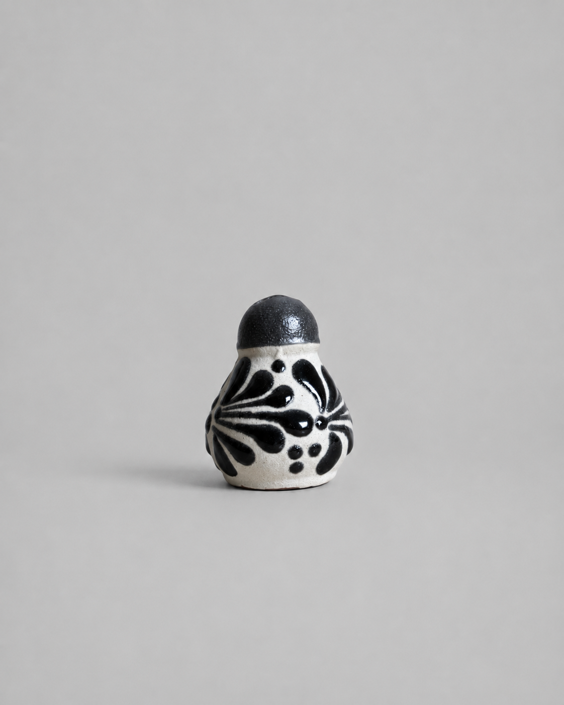 Small ceramic salt shaker with black floral patterns on a gray background