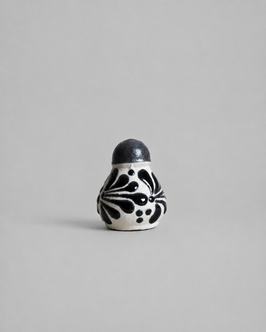 Small ceramic salt shaker with black floral patterns on a gray background
