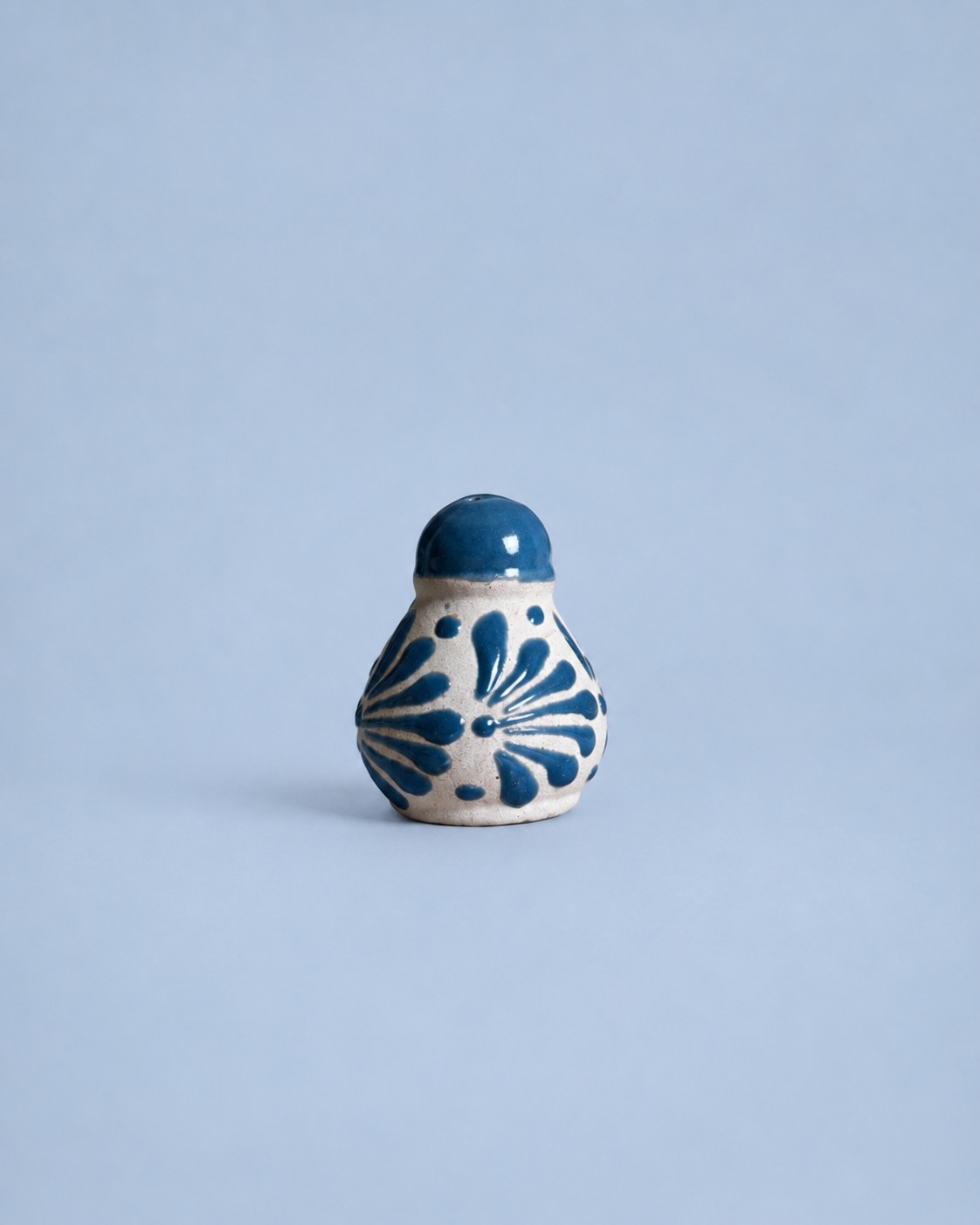 Small ceramic salt shaker with blue floral patterns on a light blue background