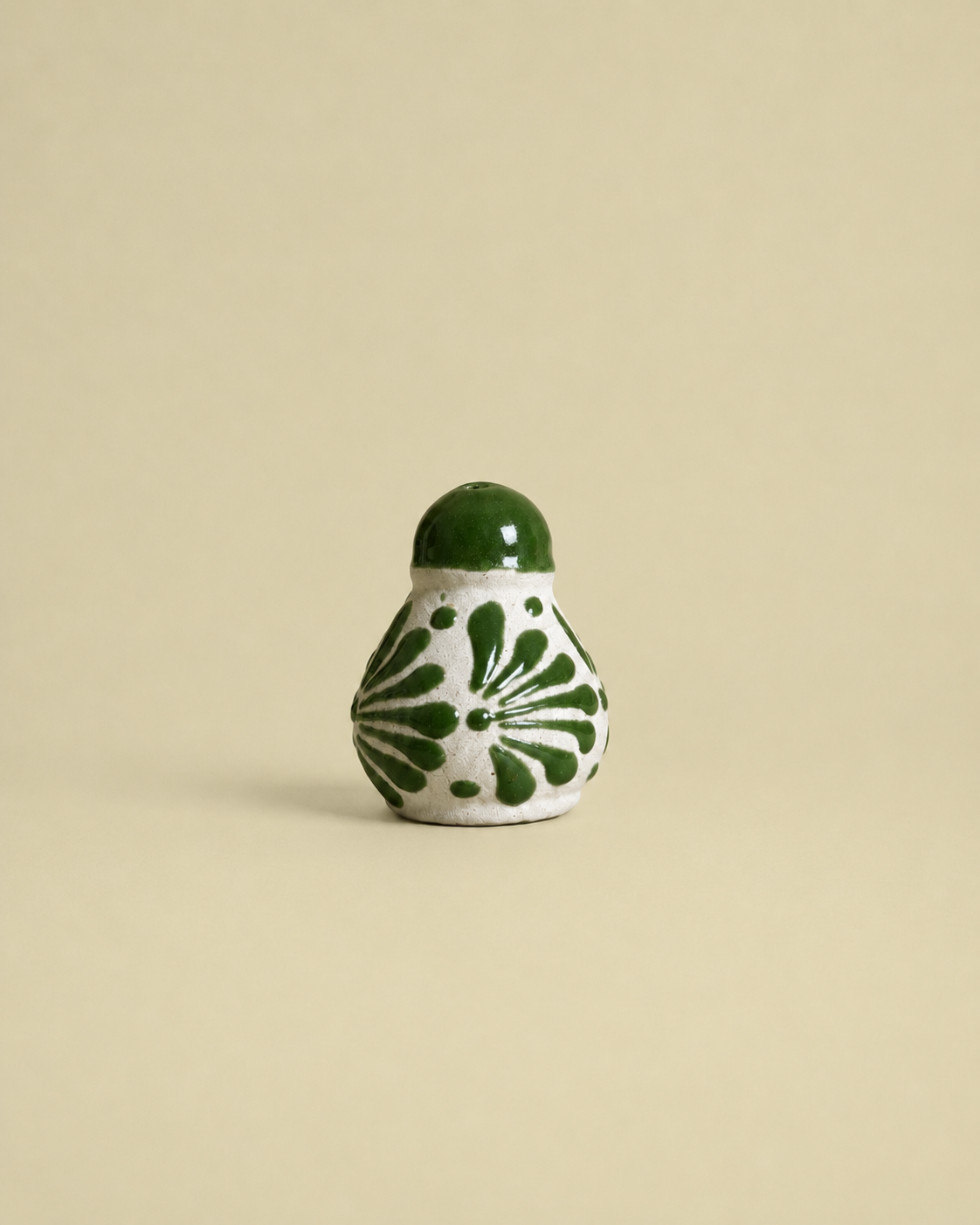 Small ceramic salt shaker  with green floral patterns on a beige background