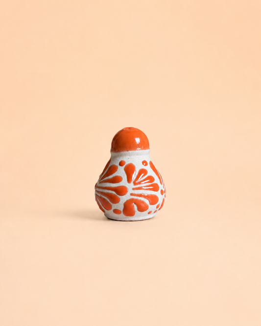 Decorative ceramic salt shaker with orange and white pattern on a beige background