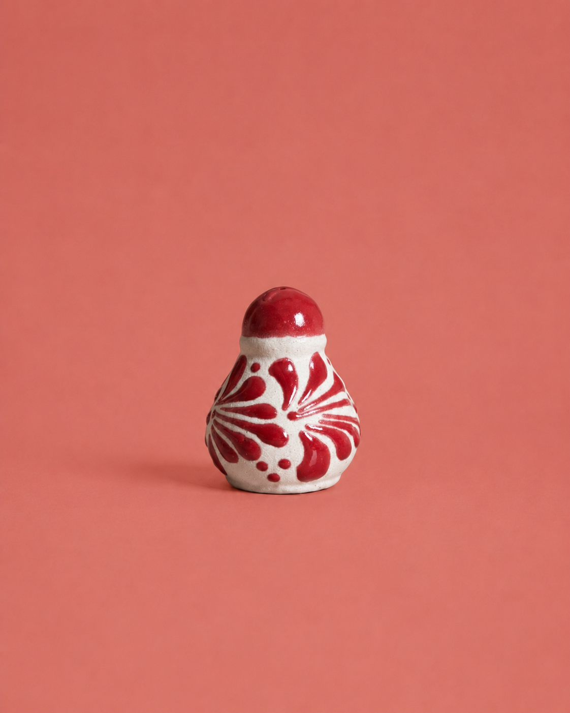 Small ceramic salt shaker with red and white pattern on a coral background