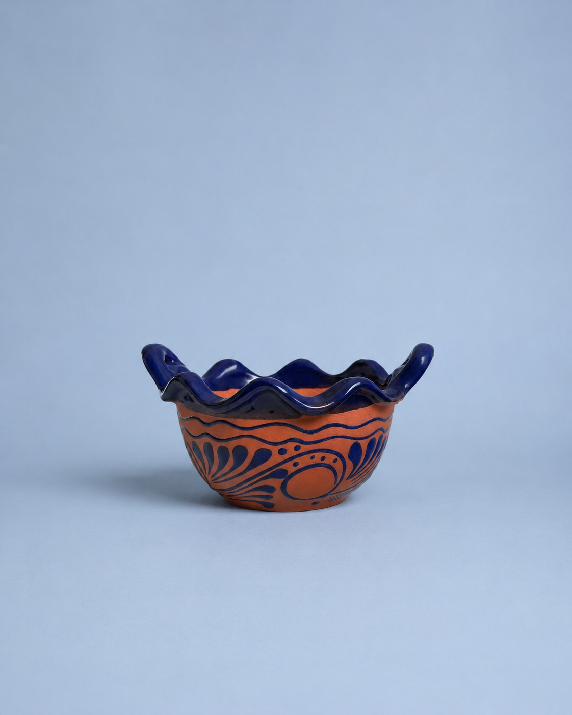 Ceramic bowl with blue rim and orange interior on a light blue background