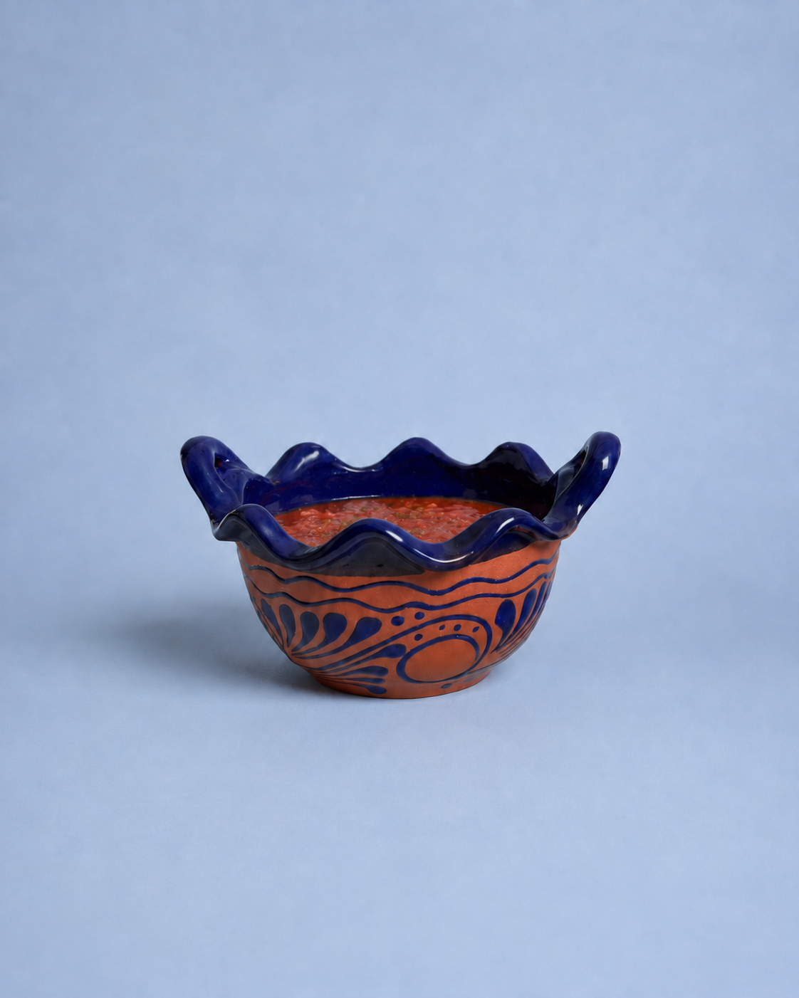 Ceramic bowl with blue rim and orange interior on a light gray background