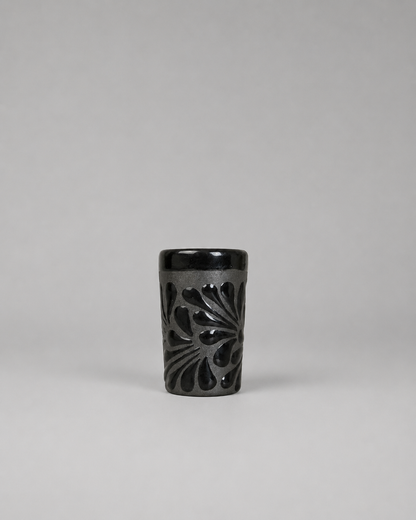 Black ceramic shot glass with floral patterns on a gray background