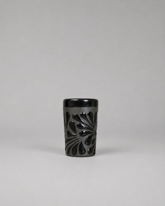 Black ceramic shot glass with floral patterns on a gray background