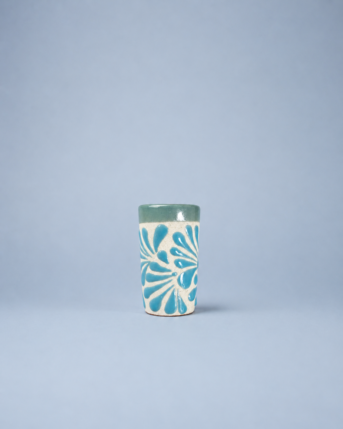 Ceramic shot glass with blue floral pattern on a light gray background