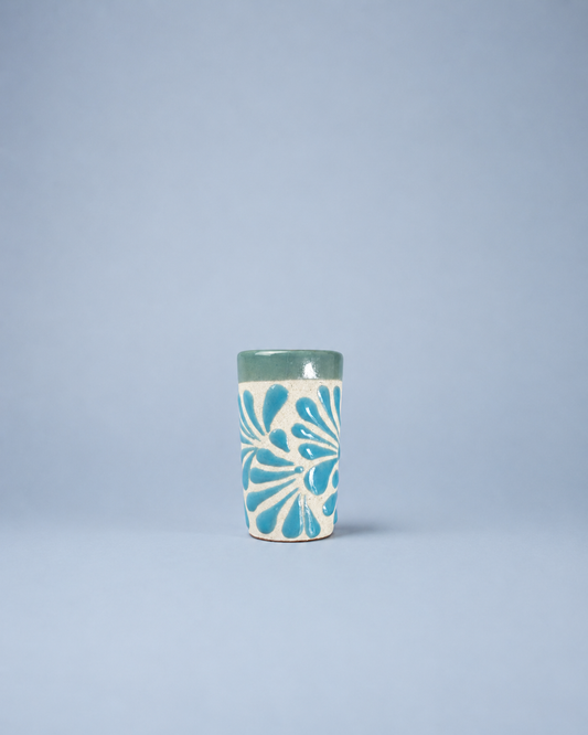 Ceramic shot glass with blue floral pattern on a light gray background
