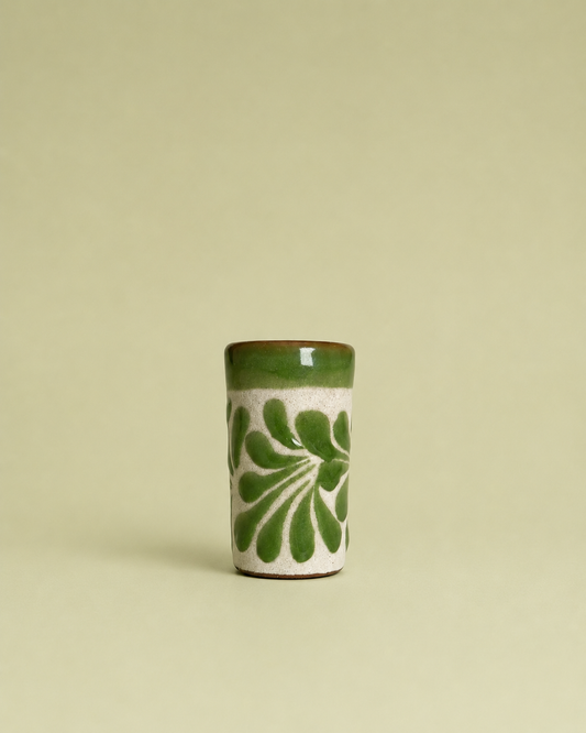Ceramic shot glass with green floral design on a beige background