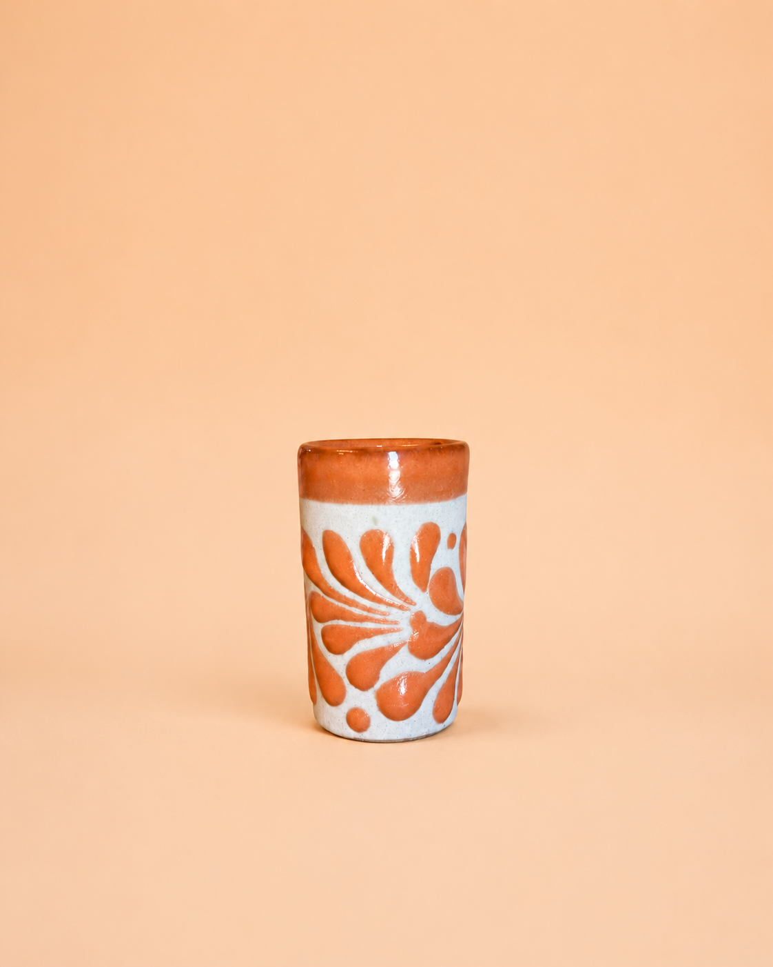 Ceramic shot glass with orange floral design on a beige background