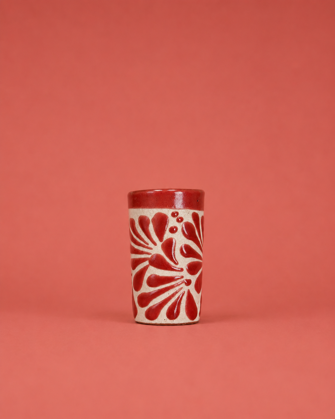 Ceramic shot glass with red floral pattern on a coral background