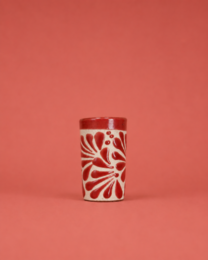 Ceramic shot glass with red floral pattern on a coral background