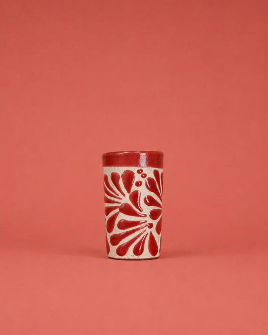 Ceramic shot glass with red floral pattern on a coral background