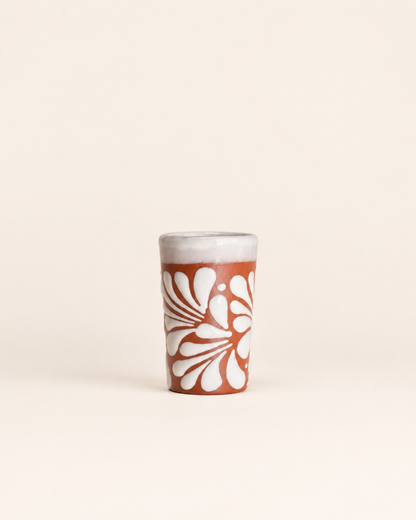 Ceramic shot glass with white floral design on a beige background