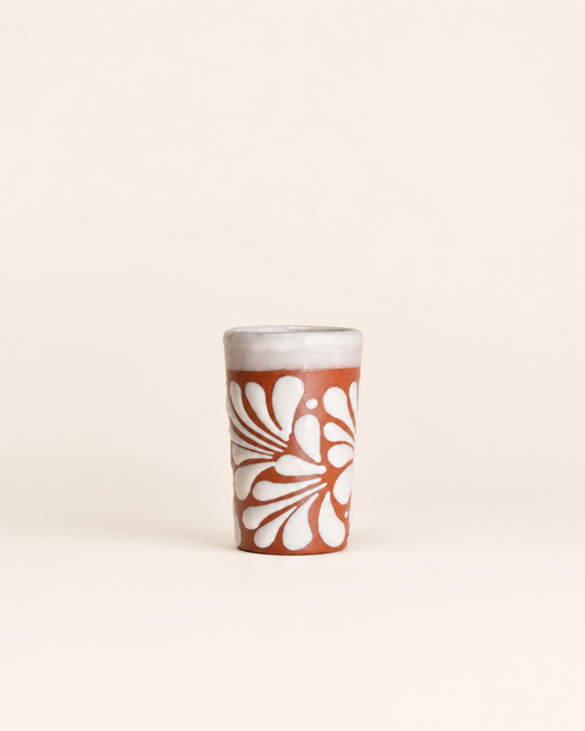 Ceramic shot glass with white floral design on a beige background