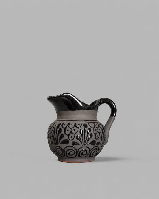 Ceramic pitcher with black floral patterns on a gray background