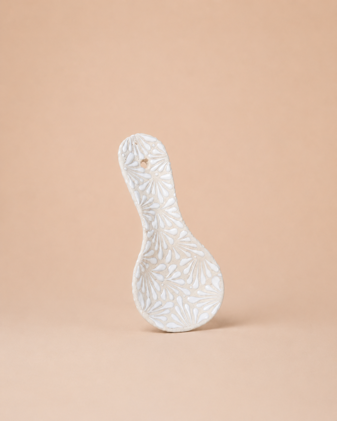 White ceramic spoon rest with floral patterns on a beige background