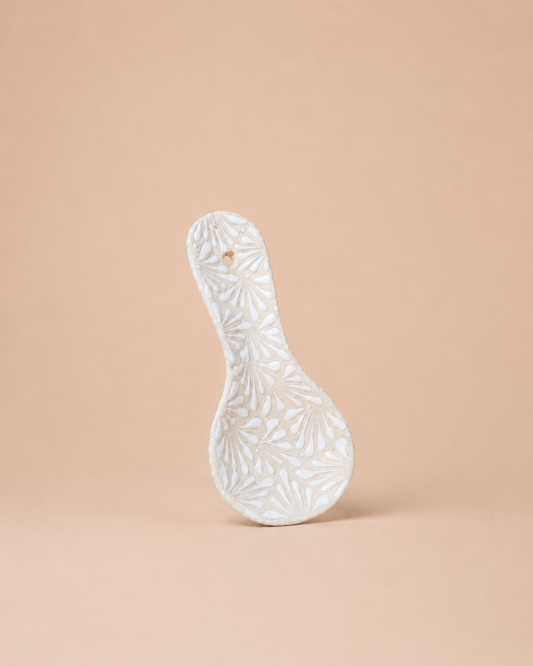White ceramic spoon rest with floral patterns on a beige background