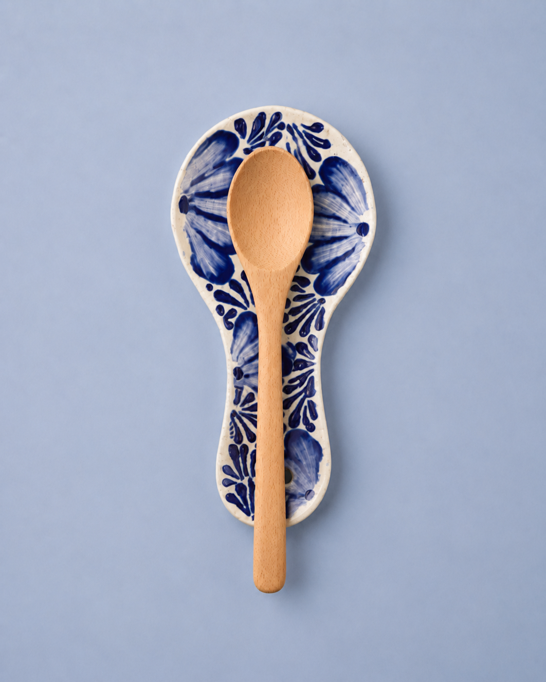 Wooden spoon in a ceramic holder with blue floral patterns on a light blue background