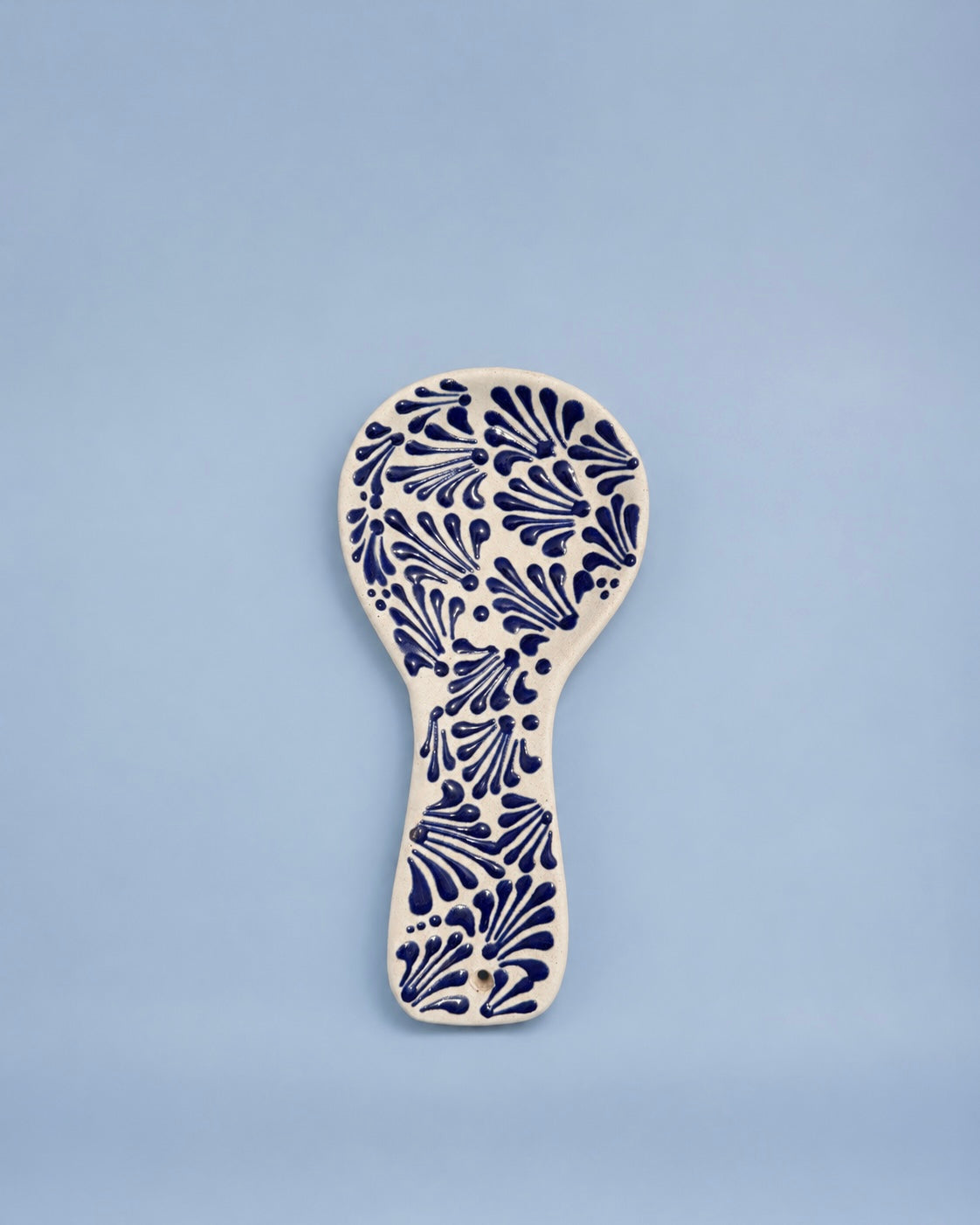 A ceramic spoon rest with a navy blue floral pattern on an off-white base, centered against a solid light blue background.