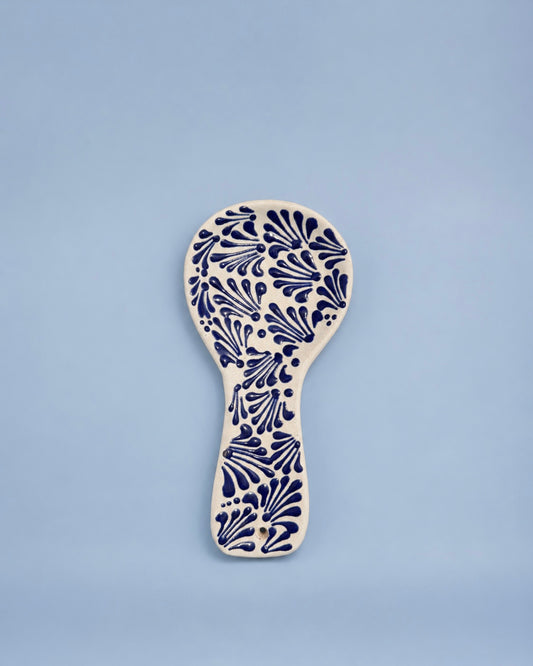 A ceramic spoon rest with a navy blue floral pattern on an off-white base, centered against a solid light blue background.
