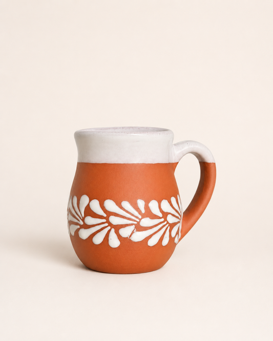 A terracotta-colored ceramic mug with a white floral pattern and a white interior, set against a solid cream background.
