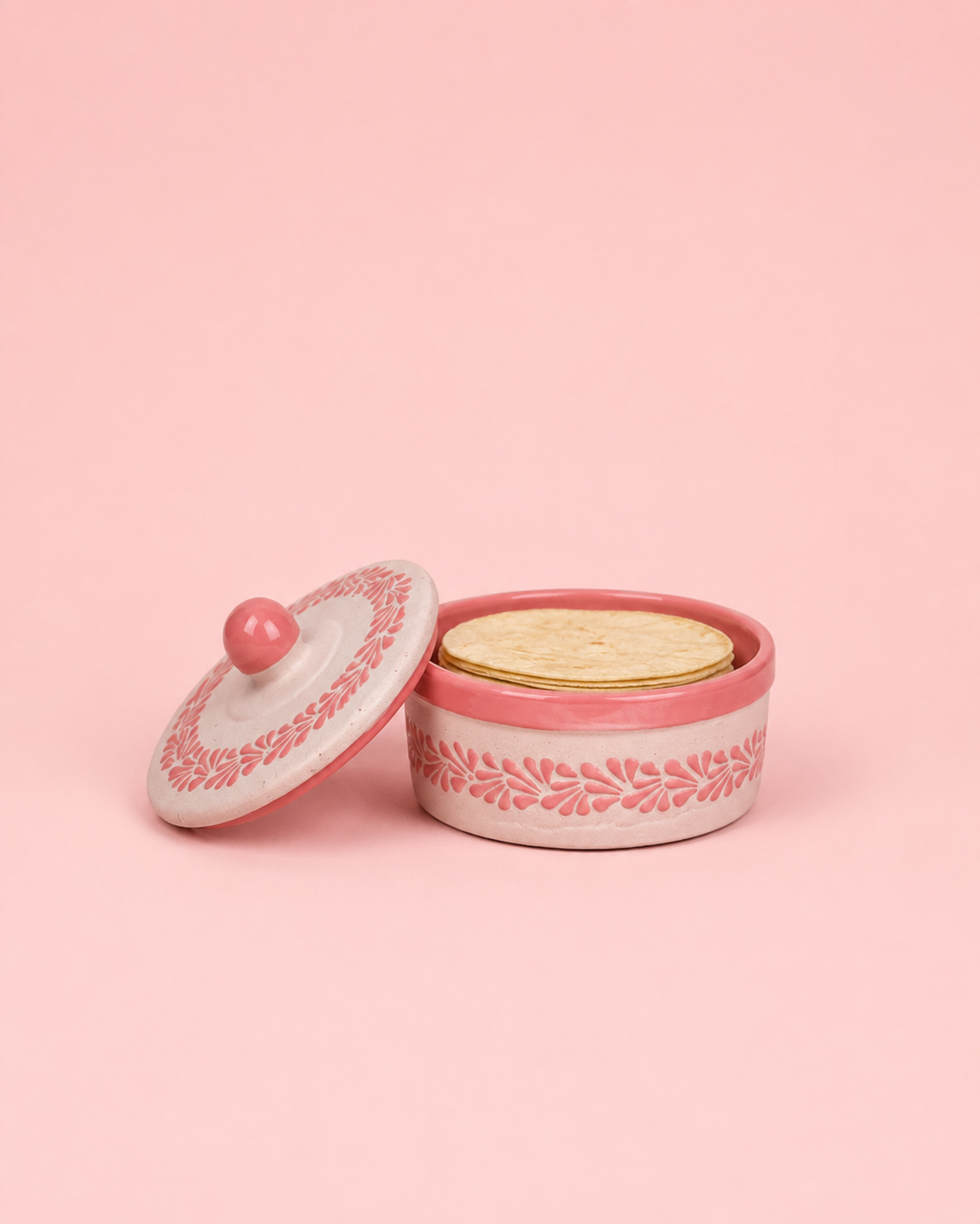 Pink ceramic container with lid on the side and tortillas inside on a pink background