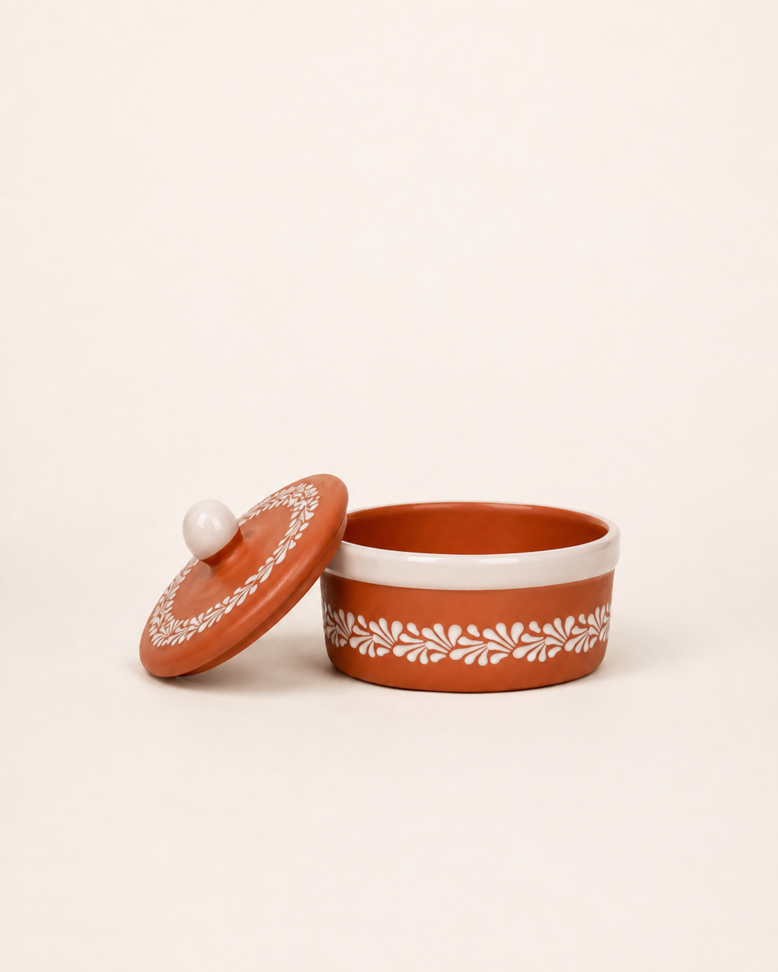 Terracotta container with white lid and decorative patterns on a beige background
