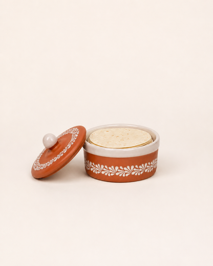 Decorative ceramic container with lid on the side and tortillas inside on a white background