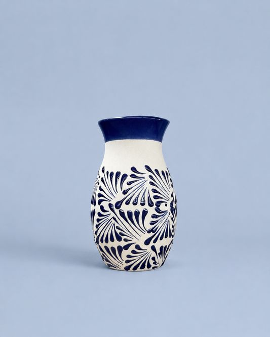 A small ceramic vase with a cream body, dark blue patterned floral design, and a solid dark blue rim, set against a solid light blue background.
