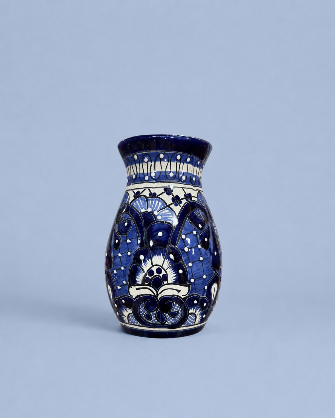 A small ceramic vase with a cobalt blue and white hand-painted floral pattern, set against a solid light blue-gray background.
