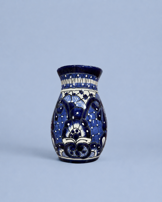 A small ceramic vase with a cobalt blue and white hand-painted floral pattern, set against a solid light blue-gray background.