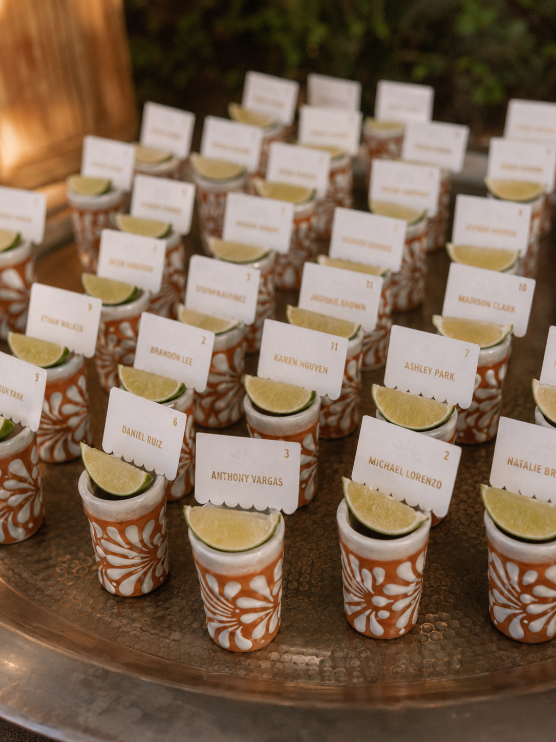 Decorative shot glasses with lime slices and name cards on a metallic tray