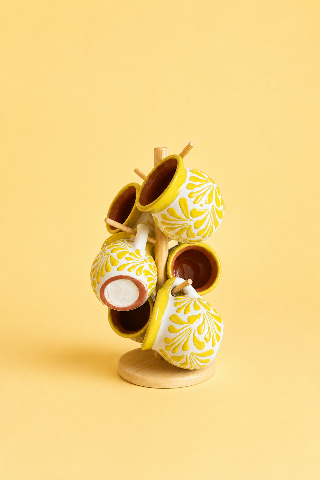 6 white mugs with yellow floral pattern on a stand, on a light yellow background